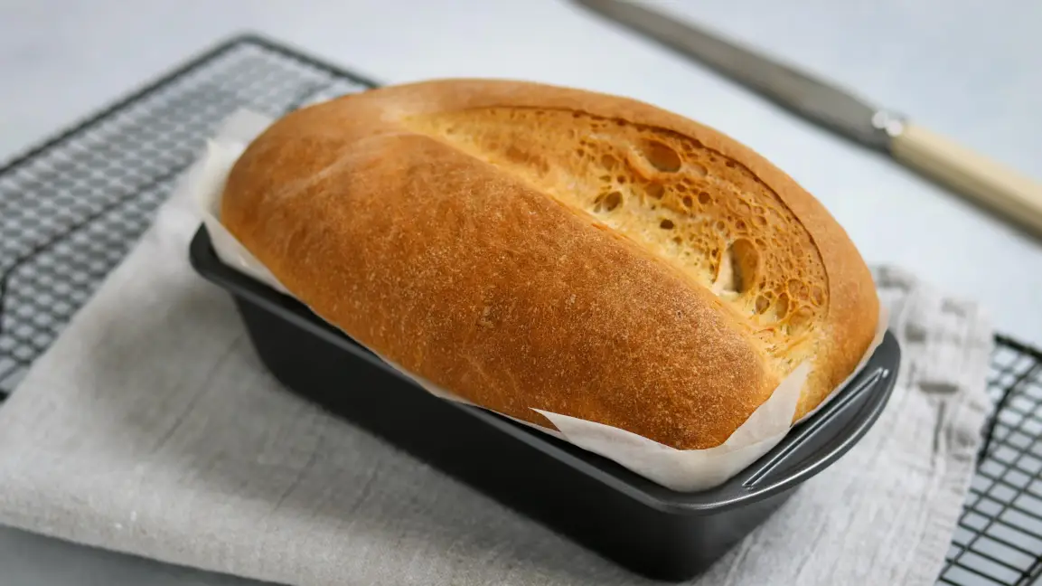 Golden brown homemade loaf cooling in a bread tin lined with non-stick baking paper for easy release and clean baking results