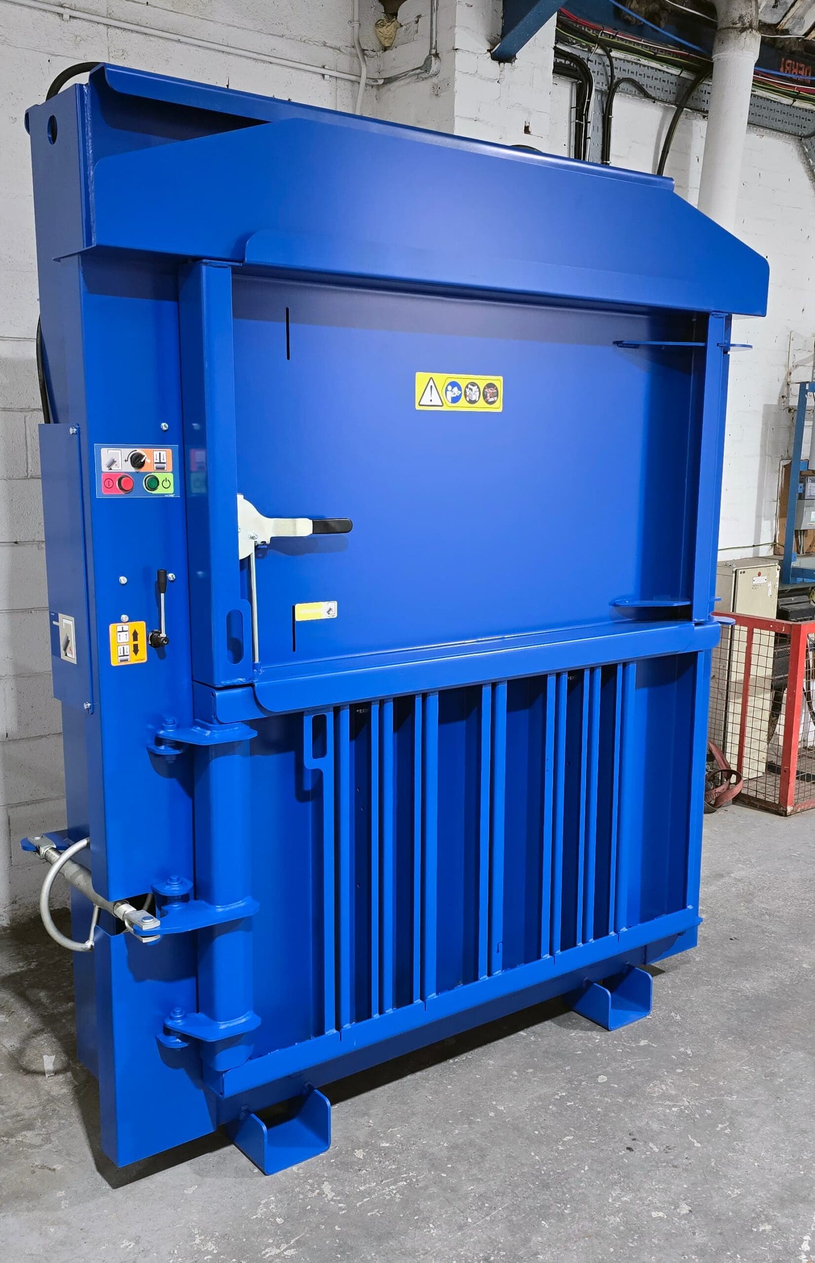Blue Macfab 550 vertical baler compacting cardboard and plastic waste in an industrial warehouse.