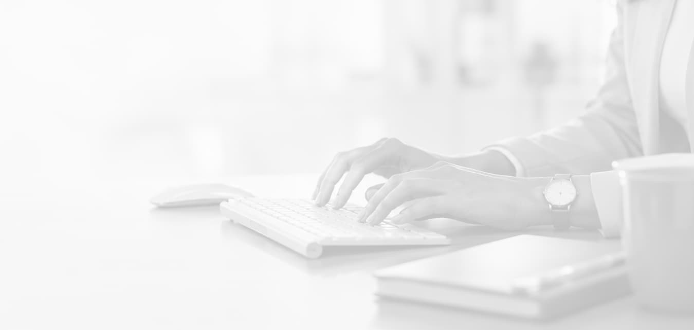 Contact Us - Close-up of a person typing on a keyboard at a bright office desk, with a mouse and stacked notebooks nearby.